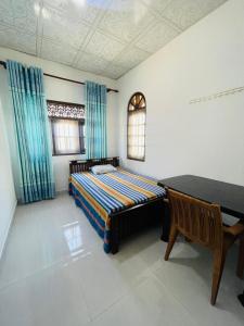 a bedroom with a bed and a table and blue curtains at Dream Villa Homestay Madiha in Matara