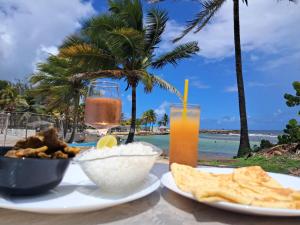 a table with food and a drink on the beach at Le Nid d'Amour Créole - Studio romantique avec accès au lagon et à la piscine XXL de 1 000 m2 - Saint-François in Saint-François
