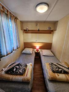 2 camas en una habitación pequeña con lámpara en MOBIL HOME DANS CAMPING 3 etoiles GORGES DU VERDON CALME 4 PERS PLANCHA, en Sainte-Croix-du-Verdon 1 foto más