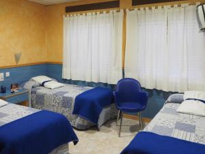 a bedroom with two beds and a blue chair at Hostal El Cartero in Teruel