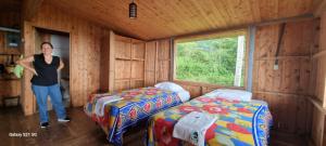 a woman standing in a room with two beds at Cabaña con vistas al bosque de Platanillo y al océano Pacífico in Magnolia