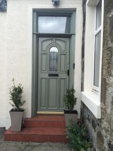 eine grüne Tür auf einem Haus mit zwei Topfpflanzen in der Unterkunft The Haven Cottage in Slamannan