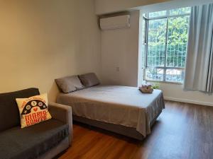 a bedroom with a bed and a couch and a window at Studio SDU Aeroporto VLT Metrô Cinelândia in Rio de Janeiro