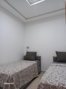 two beds and a couch in a room with white walls at Rimal Costa Martil in Martil