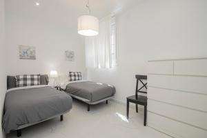 a white bedroom with two beds and a chair at NEW! Stunning modern 2BR apt next to Feria in Seville