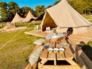 a wooden picnic table with a tent in a field at Quex Glamping in Birchington