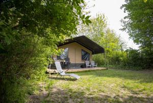 a house with a black roof and a chair in the grass at Luxe 5 persoons safaritent in Anna Paulowna