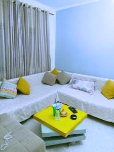 un salon avec deux lits et une table jaune dans l'établissement Ennasr 1 - appartement Charmant S1 Calme et Connecté, à Ariana