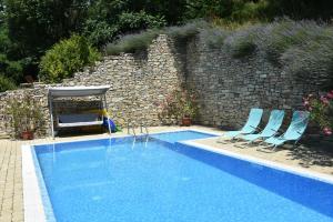 a blue swimming pool with two chairs and a stone wall at Ulbert Pince Panzió in Szederkény
