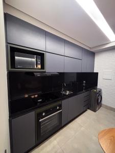 a kitchen with black cabinets and a microwave at Apartamento Loft Lazer Completo in Belo Horizonte