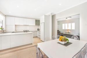 a white kitchen with a table with a bowl of fruit on it at Malibu Palms - Echuca Holiday Homes in Moama
