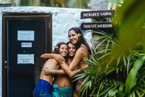three girls posing for a picture in front of a sign at Orion Healing Centre in Srithanu