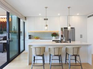 een keuken met witte kasten en barkrukken bij PineTree Penthouse by Coast Hosting in Terrigal