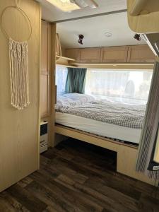 Una cama vacía en una casa rodante con ventana. en Mietwohnwagen 2 Personen, en Behrensdorf
