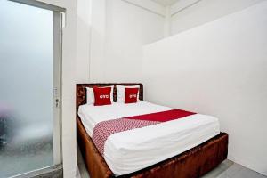 un lit avec des oreillers rouges dans une chambre blanche dans l'établissement Hotel O Grand Syariah Hagawa Lamongan Near SPORT CENTER LAMONGAN, à Lamongan
