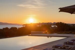 a sunset over a swimming pool with the sun setting at Villa Dafni Tinos in Agios Fokas