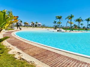a large swimming pool next to a beach with palm trees at Villa Almendro Santa Rosalia Lake and Life Resort by PREMIUM SPAIN PROPERTIES in Torre-Pacheco