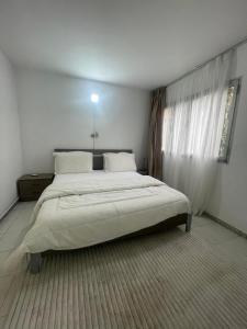a large bed in a white bedroom with a window at Appartement T3 in Abidjan