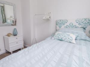 a white bedroom with a bed and a dresser at 3 Glyn Y Mor in Pwllheli