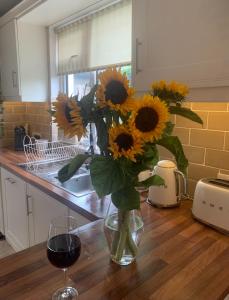 eine Vase mit Sonnenblumen auf einem Tisch mit einem Glas Wein in der Unterkunft 3 Bedroom house in Dublin in Lucan