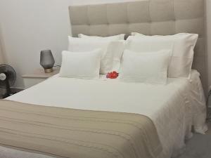 a white bed with white pillows and a red flower on it at My home in Cercal