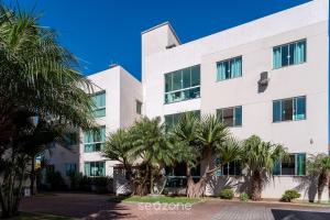 a white building with palm trees in front of it at Apto 2 Quartos c/ Ar a 270m da Praia GPS0102 in Imbituba