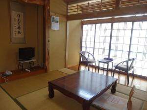 een woonkamer met een tafel en stoelen en een televisie bij Ishibu-so in Matsuzaki