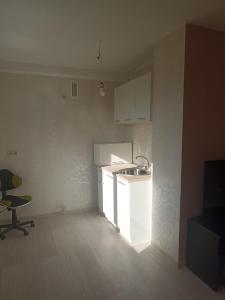 una cucina con armadi bianchi, lavandino e sedia di Divu istabu saulains dzīvoklis Ugālē a Ugāle