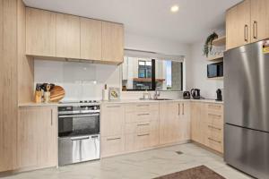 une cuisine avec des armoires en bois et un réfrigérateur en acier inoxydable dans l'établissement Well-styled Vibrant 2 Bed Home, à Auckland