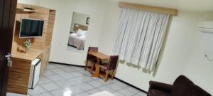 a living room with a table and a room with a bed at Goldmen Business Criciúma in Criciúma