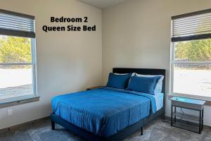 a bedroom with a bed with a blue comforter and two windows at Brand New Yote Cabin, Pool Table, South of Norman in Purcell +27 photos