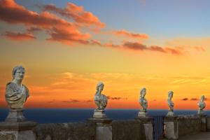 einen Steinzaun mit Statuen und Blick auf den Ozean bei Sonnenuntergang in der Unterkunft Hotel Villa Cimbrone in Ravello