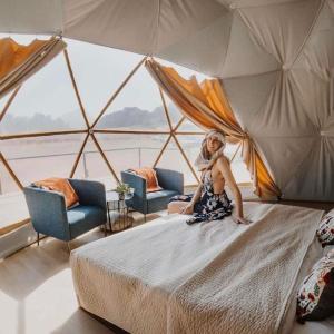 a woman sitting on a bed in a room at Traditions of Wadi Rum camp & jeep tour in Wadi Rum