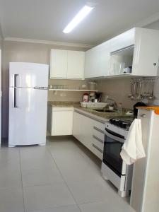 a kitchen with white cabinets and a white refrigerator at Apartamento Avenida Wilson in Ubatuba