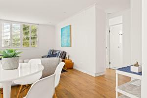 a white living room with a white table and chairs at Coastal 2-Bed Apartment Steps from Manly Beach in Sydney