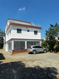 a car parked in front of a white house at Hermoso Apartamento en 3er nivel con terraza privada in Bonao