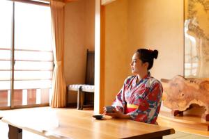 une femme assise à une table dans une pièce dans l'établissement River Side Maruyama, à Toyooka