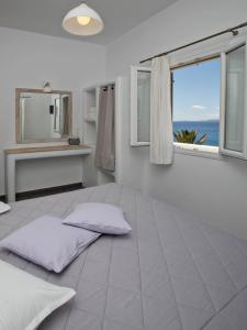 a white bedroom with two pillows on a bed with a window at Porto Raphael Residences & Suites in Agios Ioannis