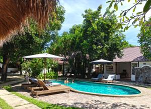 a pool with chairs and umbrellas next to a house at Si Pitung Village in Gili Islands