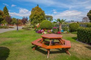 a wooden picnic table in a park with flowers at Middle Park Motel in Blenheim