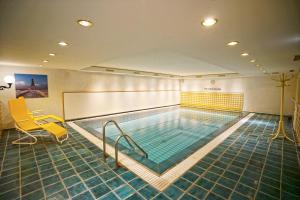 a swimming pool in a room with a yellow chair and a chair at Hotel Appartement Landhaus Stutzi - Hotel Strandperle in Cuxhaven