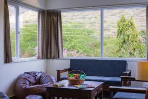 a living room with a couch and a chair and two windows at Alaya Stays Kodiyat 4-BHK Pet-Friendly Villa With Views of Sajjangarh Palace in Nāi +63 photos