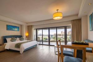 a bedroom with a bed and a desk and a balcony at Poly Phoenix Hotel in Sanya