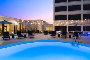 a pool in front of a building with chairs and umbrellas at Wyndham Indianapolis Airport in Indianapolis