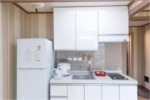 cocina con armarios blancos y nevera blanca en Cable Car Pension, en Yeosu