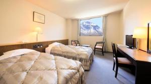 a hotel room with two beds and a desk at Kamikochi Taishoike Hotel in Matsumoto