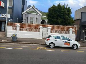 a white car parked in front of a white fence at Biscuit Mill Woodstock Backpackers in Cape Town