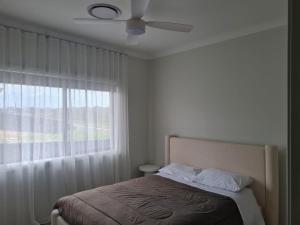 a bedroom with a bed with a ceiling fan and a window at Songlark Street, 54 in Bermagui
