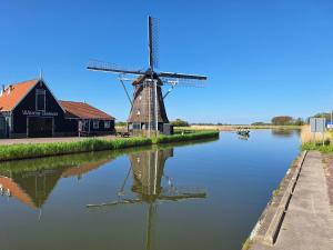 a windmill sitting on the water next to a building at Tinyhouse NATUURHUISJE met veranda Bij de Molen tussen Alkmaar en Hoorn in Oterleek