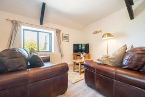a living room with two leather couches and a television at Polrunny Farm Elderberry Cottage with sea view in Boscastle
